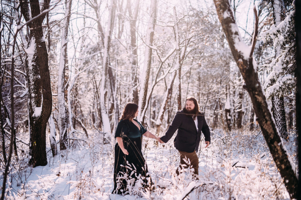 winter engagement photo inspiration of a cute couple holding hands and walking through a snow covered forest in St Louis, Missouri, perfect example of relaxed natural artistic engagement and wedding photography